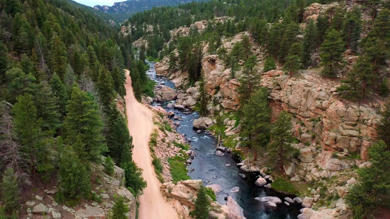 Eleven Mile Canyon — the South Platte running clear and blue-green over a rocky bed between steep granite walls, pines climbing the canyon sides, tall summer clouds overhead