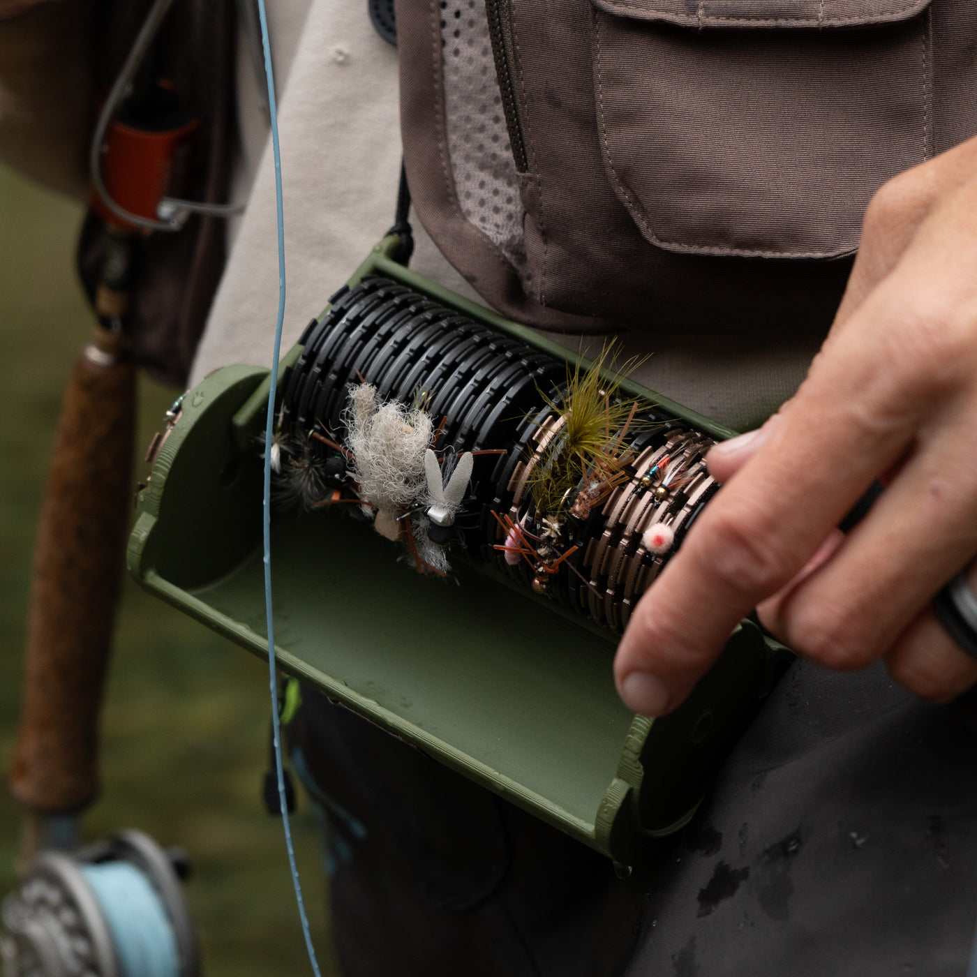 An angler on the river holding the open QuickDrift case, its spools loaded with pre-tied fly rigs, rod and reel in hand